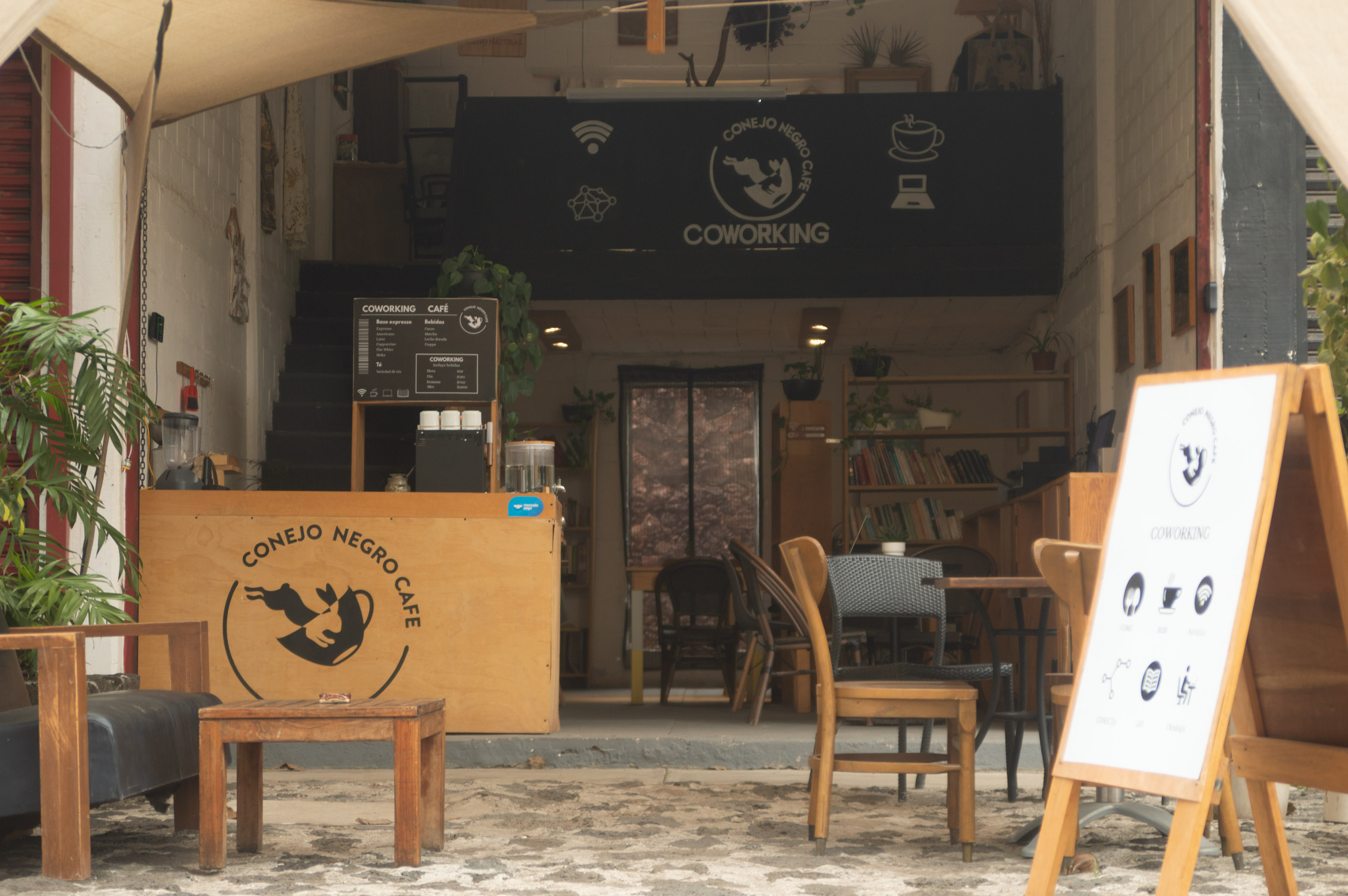 Entrada exterior de Conejo Negro Café con señalización de coworking y mesas al aire libre