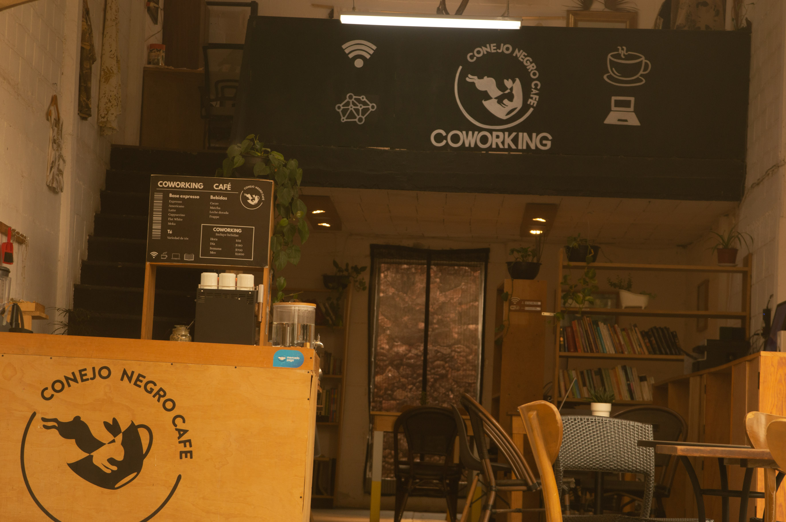 Interior de Conejo Negro Café con mesas, libreros y área de coworking bien iluminada